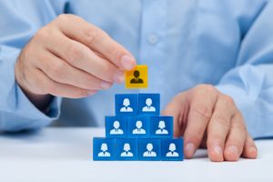 Human resources and corporate hierarchy concept - recruiter complete team by one leader person (CEO) represented by gold cube and icon.